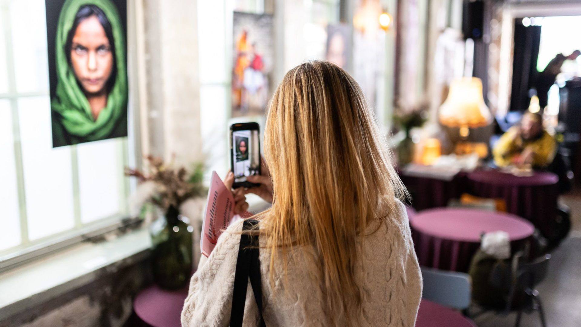 A blond woman takes a picture of a photo exhibition.