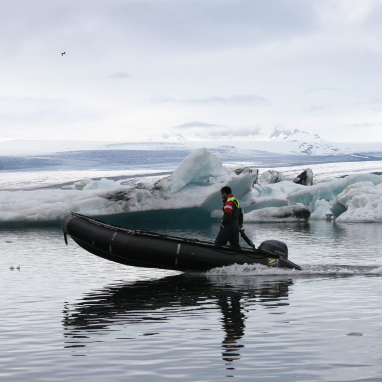 Kuvassa mies ajaa kumiveneellä sulavan jäätikön jäätikköjärvessä