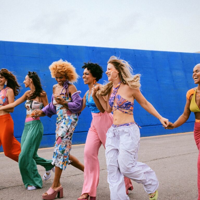 Six women in colorful clothes walking hand in hand, smiling.