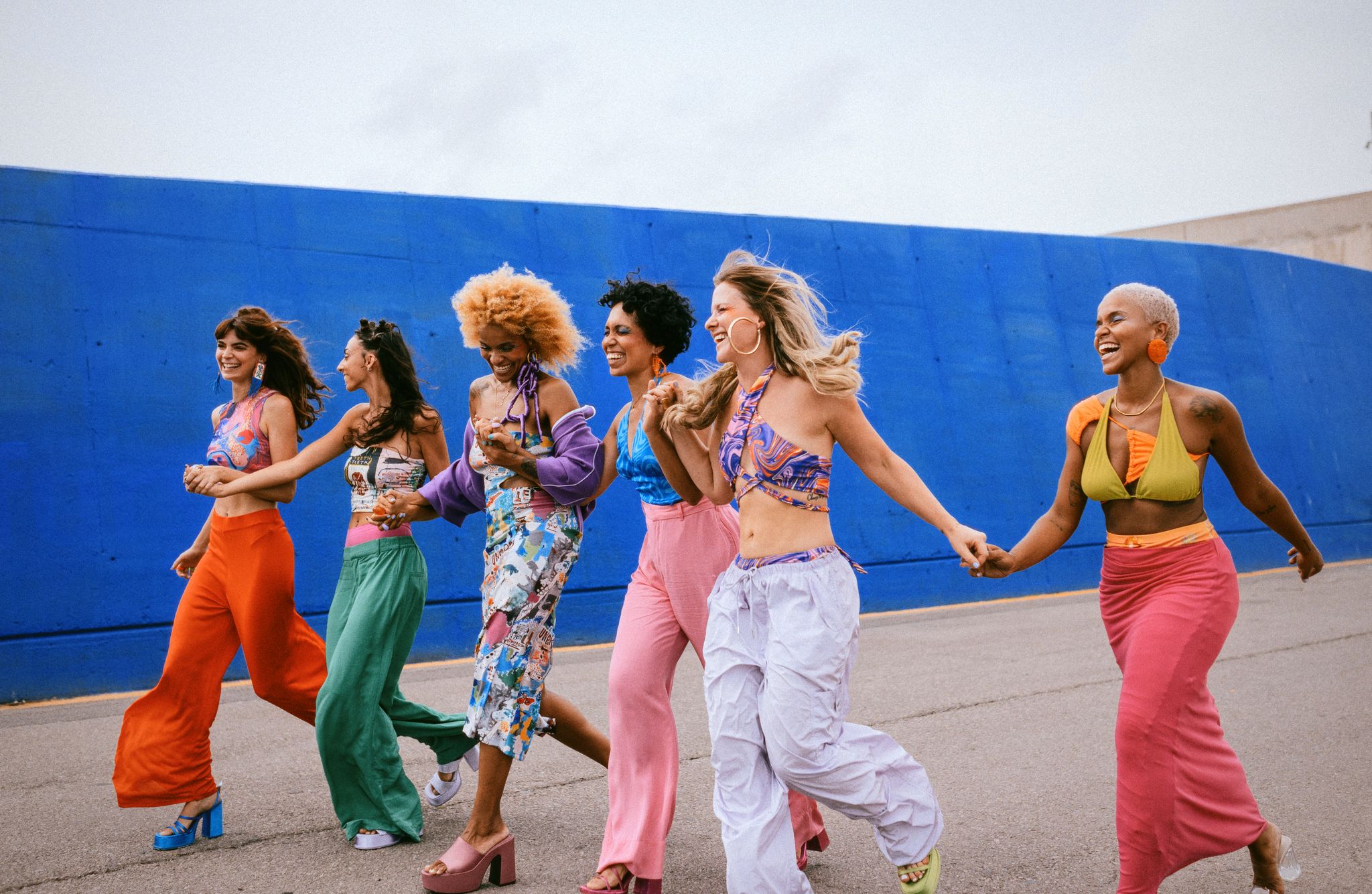 Six women in colorful clothes walking hand in hand, smiling.