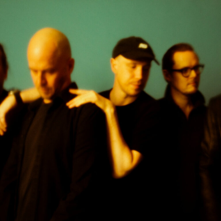 Five men dressed in black in front of a green background.