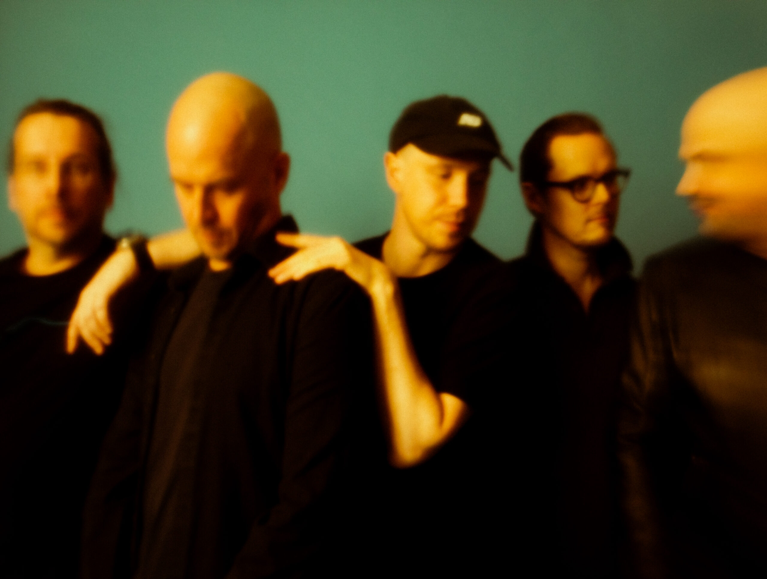 Five men dressed in black in front of a green background.