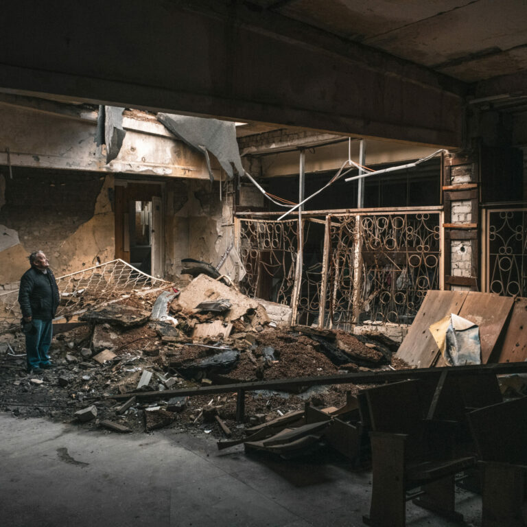 Person standing in a dim room of a collapsed building.